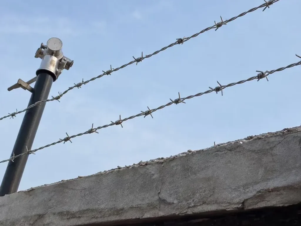 Two strands of barbed wire on a post along the top of a wall
