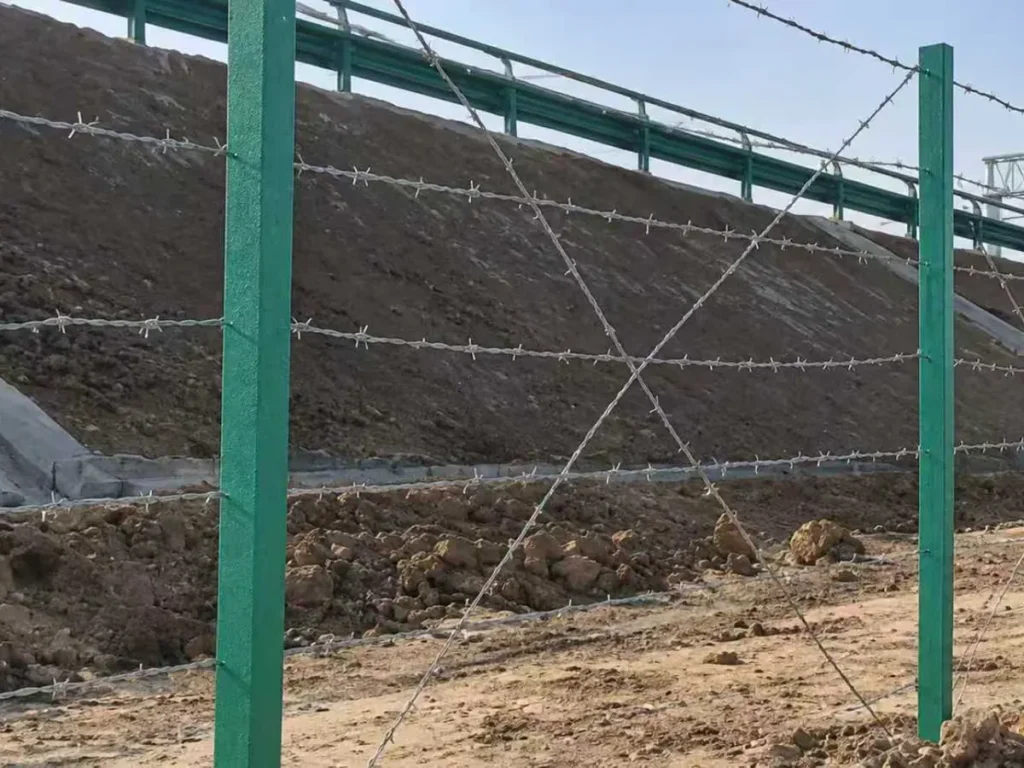 Barbed wire fence on posts along a road embankment