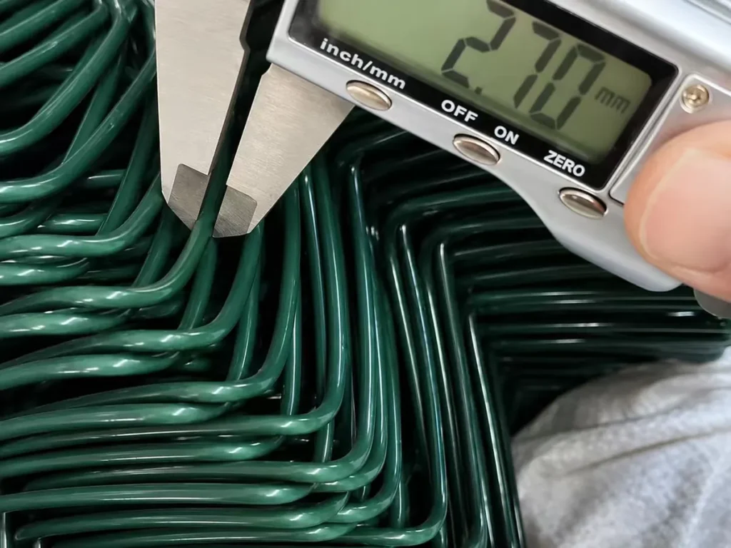 Wire diameter of green PVC-coated chain link checked with a digital caliper