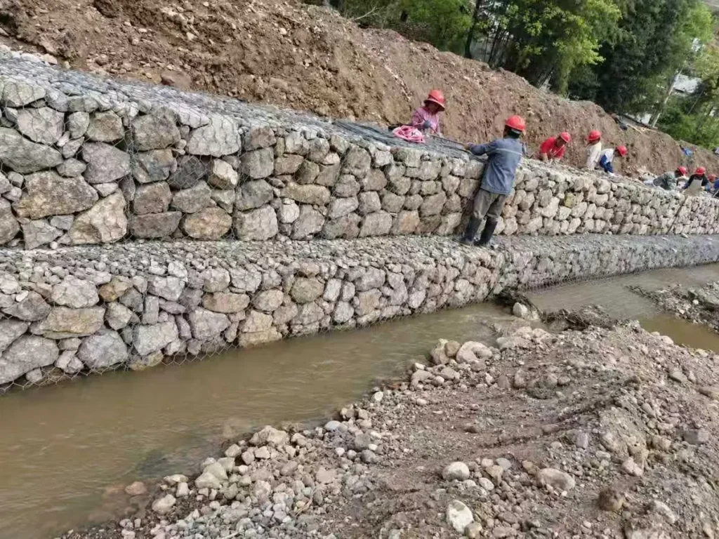 Workers building a stepped gabion retaining wall along a stream